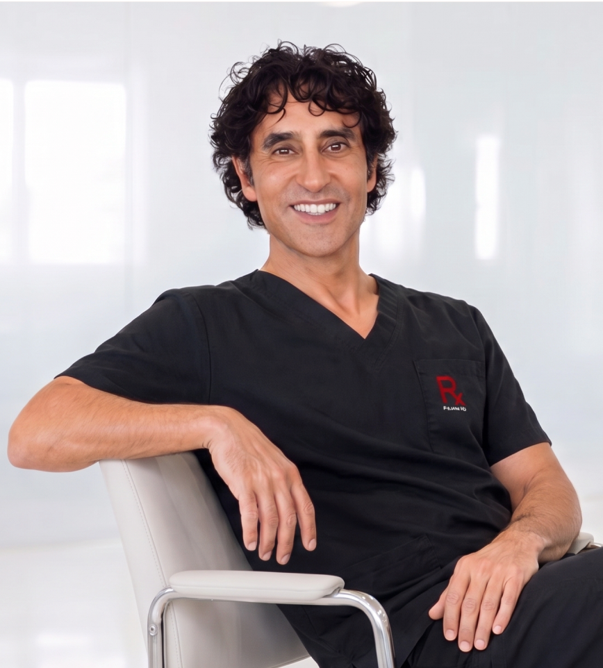 Dr. Rajani wearing black scrubs sits in a chair against a bright white background. 