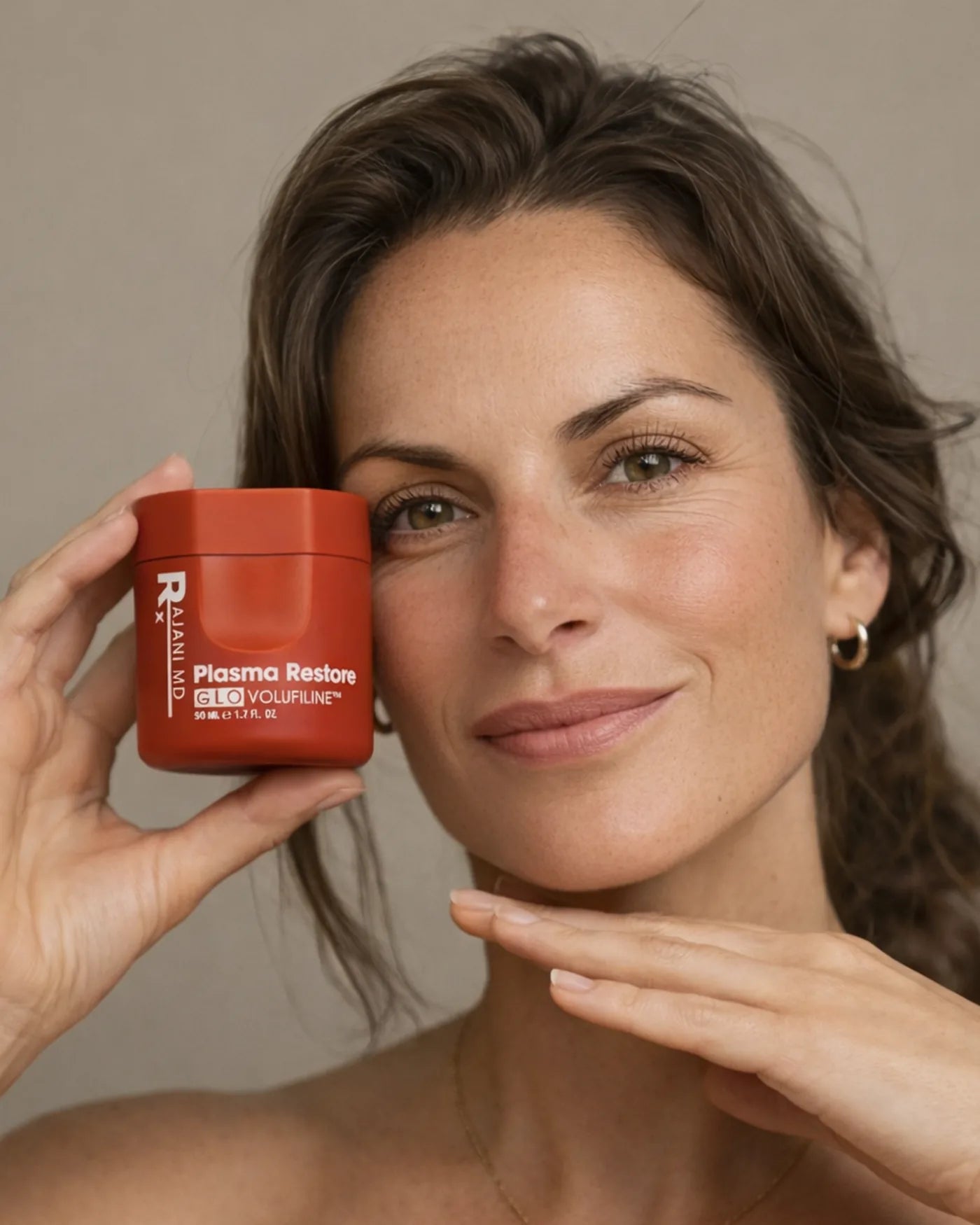 Woman holding a jar of Plasma Restore GLO Volufiline Cream beside her cheek
